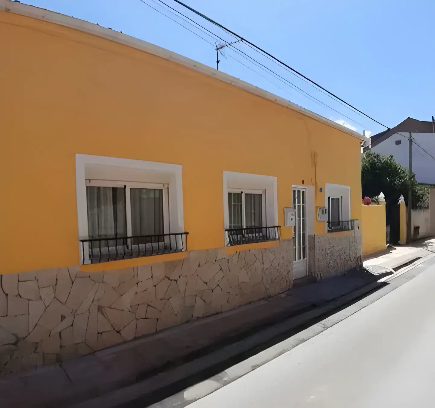 Los Pintores Cáceres Fachada de casa tradicional pintada en color amarillo con zócalo de piedra